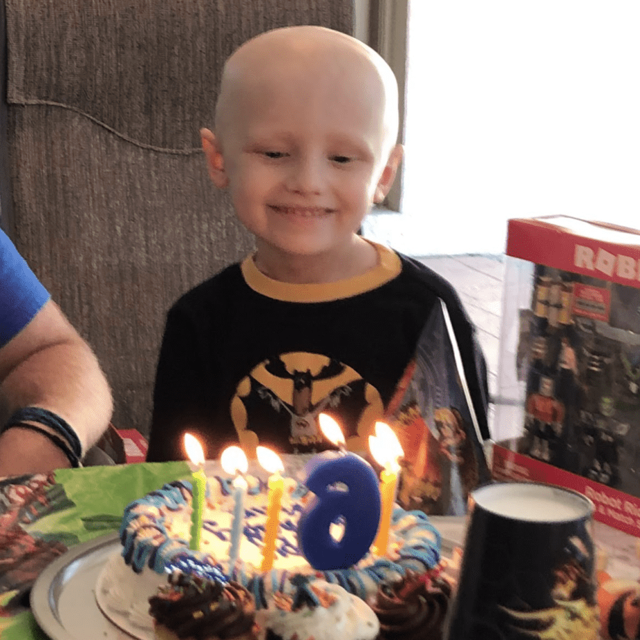 Photo of a smiling Finley Gray as he blows out his birthday candles sitting at a table in front of a cake.